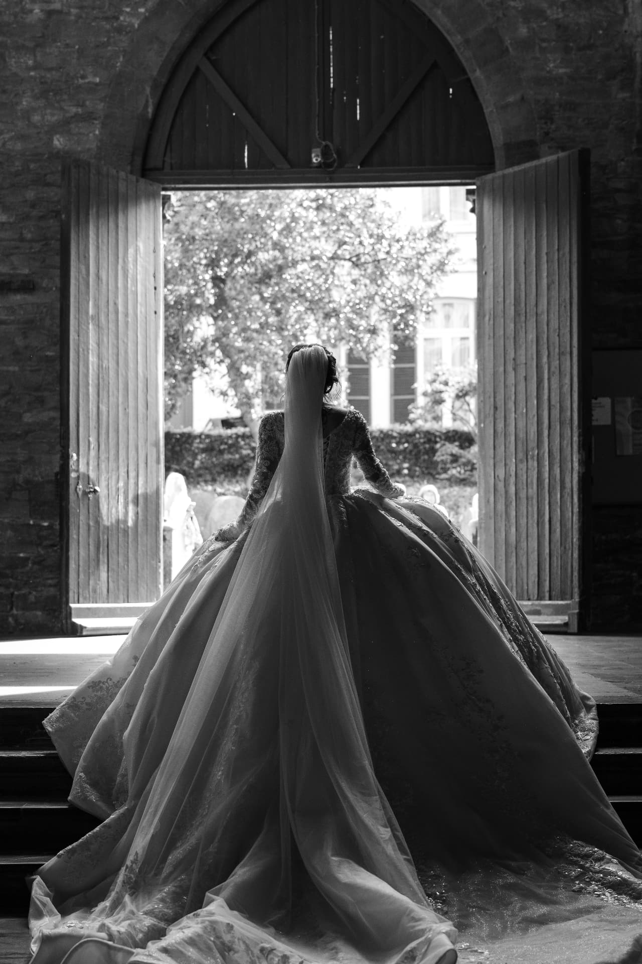 La mariée en grande robe à traîne, de dos dans la porte de la grange
