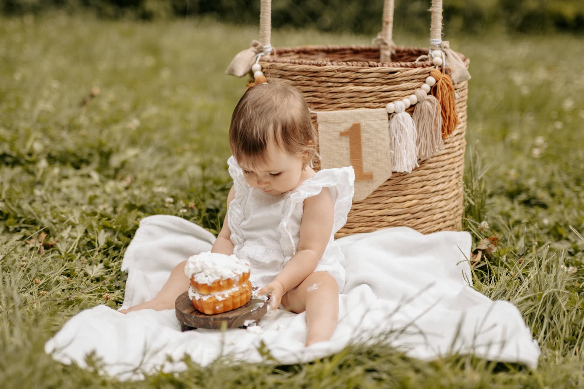 Bébé d'un an et son gâteau, assis dans l'herbe devant le panier à banderole