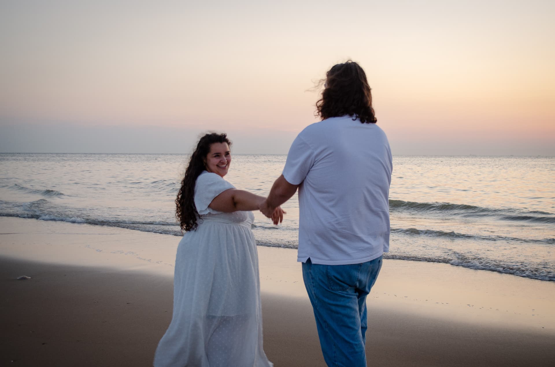 Un couple main dans la main au bord de la mer, dans la lumière douce du soir
