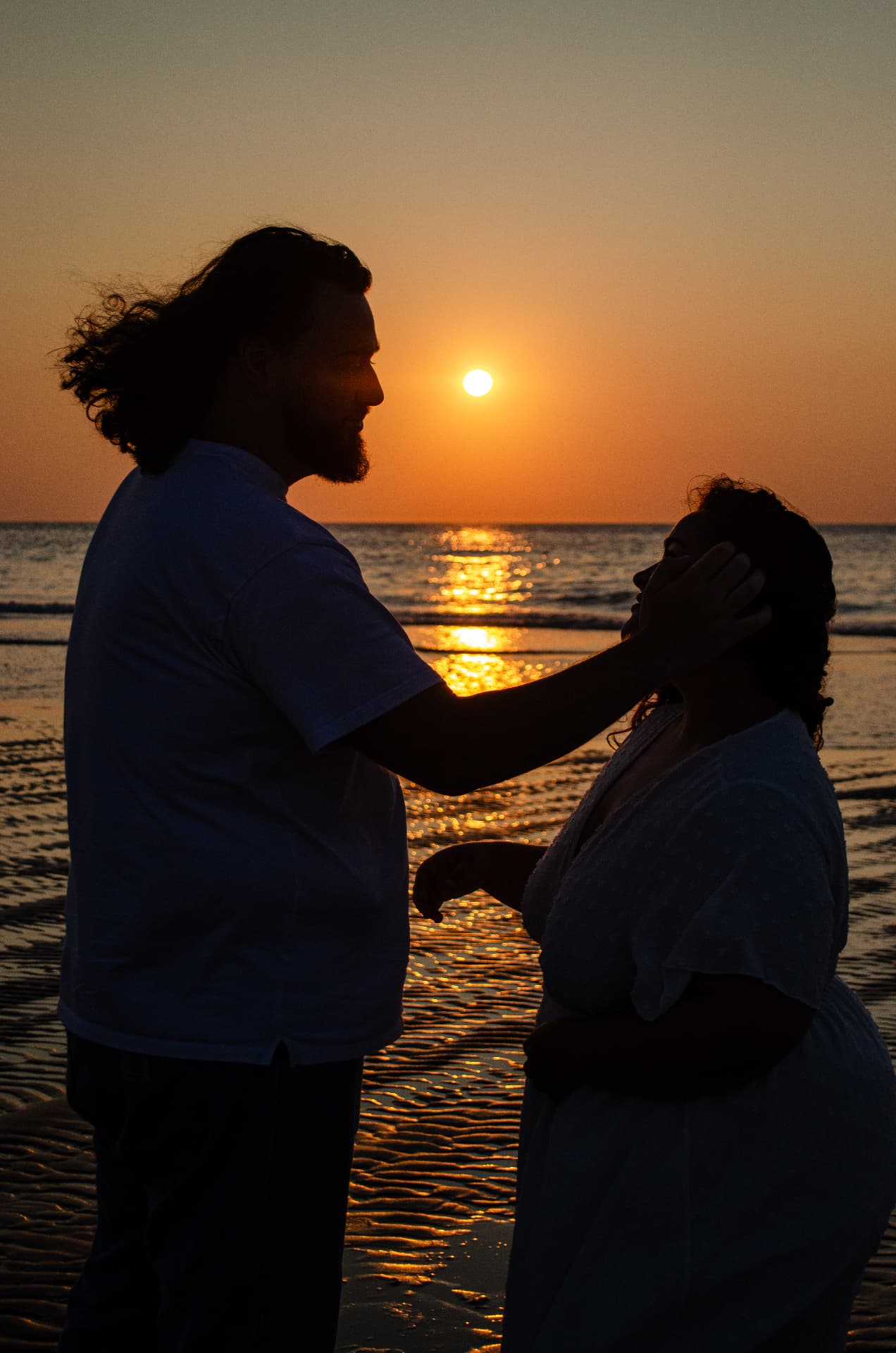 Un couple au bord de l'eau au coucher du soleil, une main sur la joue